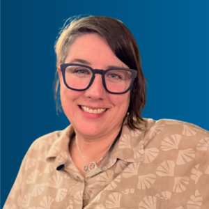 Headshot of Heather Duncan smiling, wearing dark-rimmed glasses and a patterned tan shirt, against a blue background.